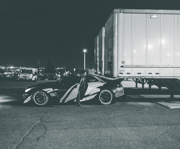 A sleek, modern car parked beside trailers at night in an urban setting.